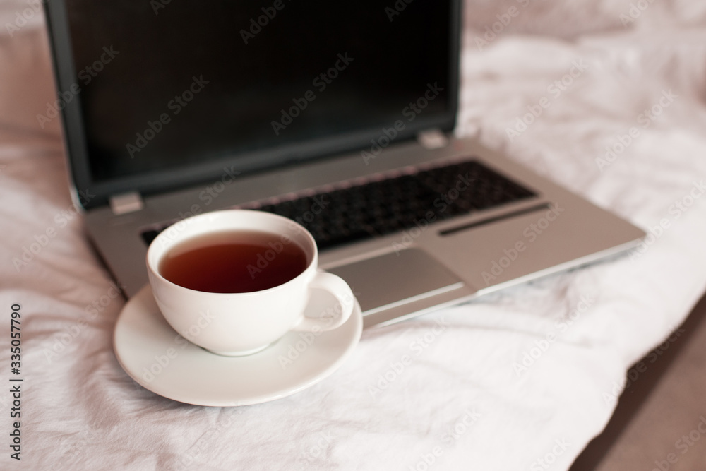 Cup of black tea on laptop in bed closeup. Quarantine time. Working at home. Good morning. Cup of black tea on laptop in bed closeup. Quarantine time. Working at home. Good morning.