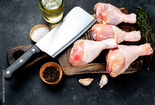 raw chicken legs with spices and meat knife on a stone background