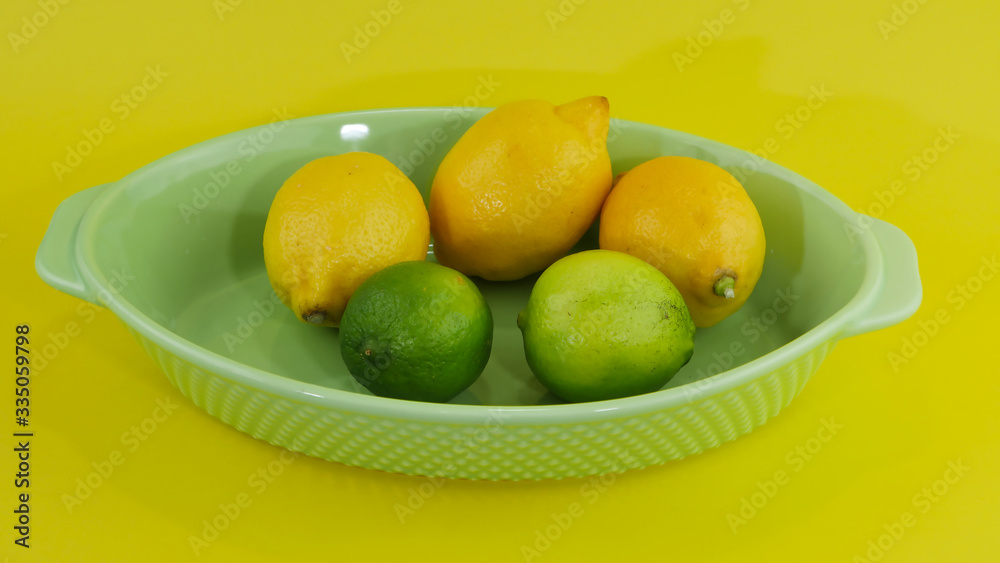 trois citrons et deux limes dans un plateau sur un arrière plan de couleur jaune