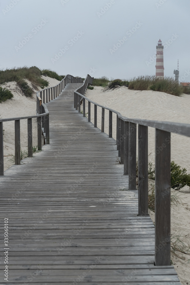 Wooden walkways along the dunes of the beach of Barra with the Aveiro lighthouse in the background in a cloudy day. Portugal