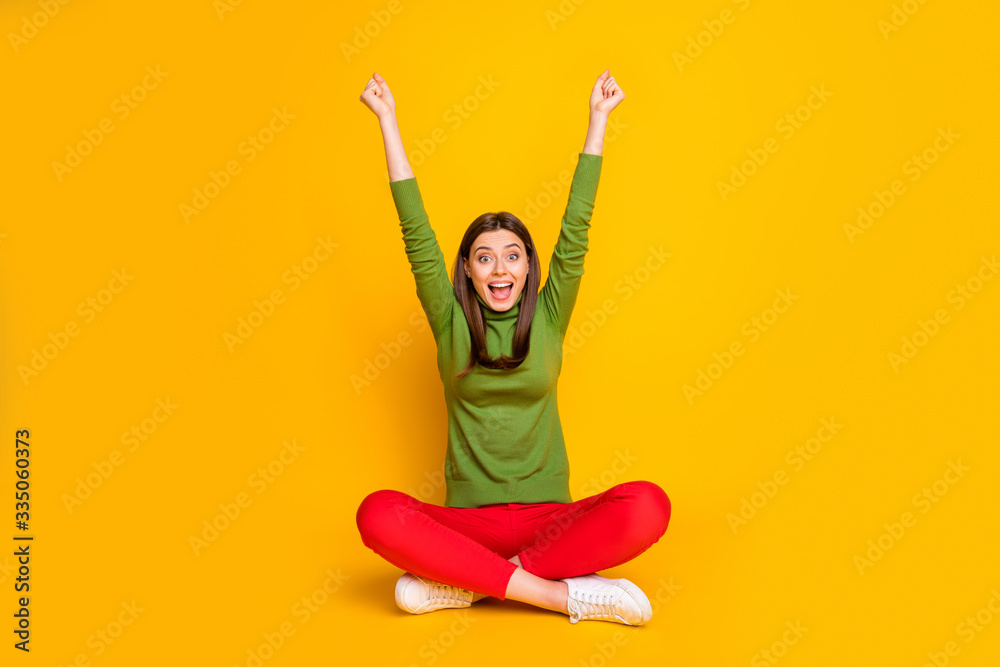 Photo of beautiful lady sit floor holding fists raised supporting favorite sports team excited cheery mood wear green sweater red trousers isolated yellow color background Photo of beautiful lady sit floor holding fists raised supporting favorite sports team excited cheery mood wear green sweater red trousers isolated yellow color background
