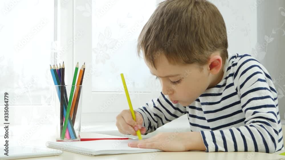A boy of preschool age, drawing with colored pencils, sitting at a table, sitting by the window. Thoughtful, intelligent child. A boy of preschool age, drawing with colored pencils, sitting at a table, sitting by the window. Thoughtful, intelligent child.