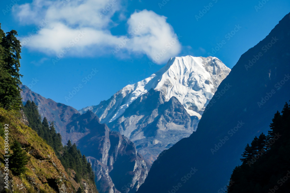 View on Himalayas, Annapurna Circuit Trek, Nepal. Early morning in the mountains. Lower parts of the mountains covered in shadow, high snow caped mountains peaks catching the first beams of sunlight