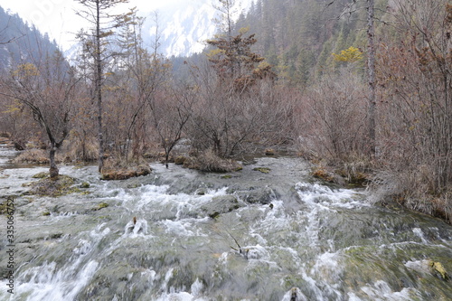 Beautiful river with crystal clear water among fall forest and scenic wooded mountains at the Valley in nature reserve (Valley National Park), China. Amazing autumn landscape.