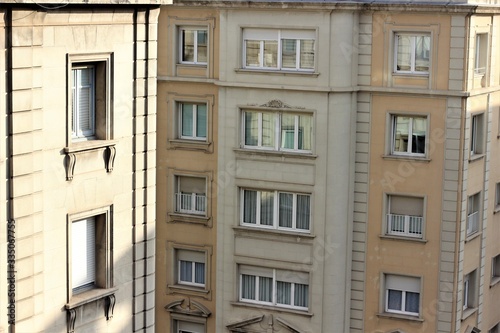 sunny windows on the upper floors of two beige buildings  one in the foreground  the second in the background.