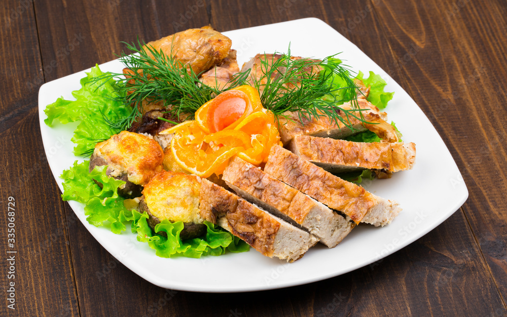 mix of chicken meat with leaves of greens, dill, cheese and a slice of orange in a square white plate on a wooden table