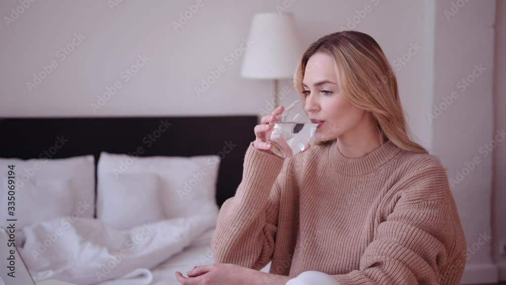 Woman works at home, looks at computer monitor and drinks water. Woman works at home, looks at computer monitor and drinks water.