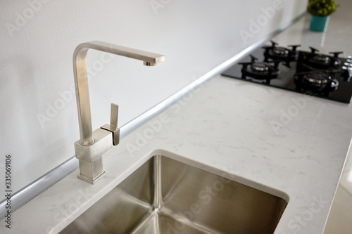 Modern design chrome water tap over stainless steel kitchen sink on table top made of stone marble or granite.