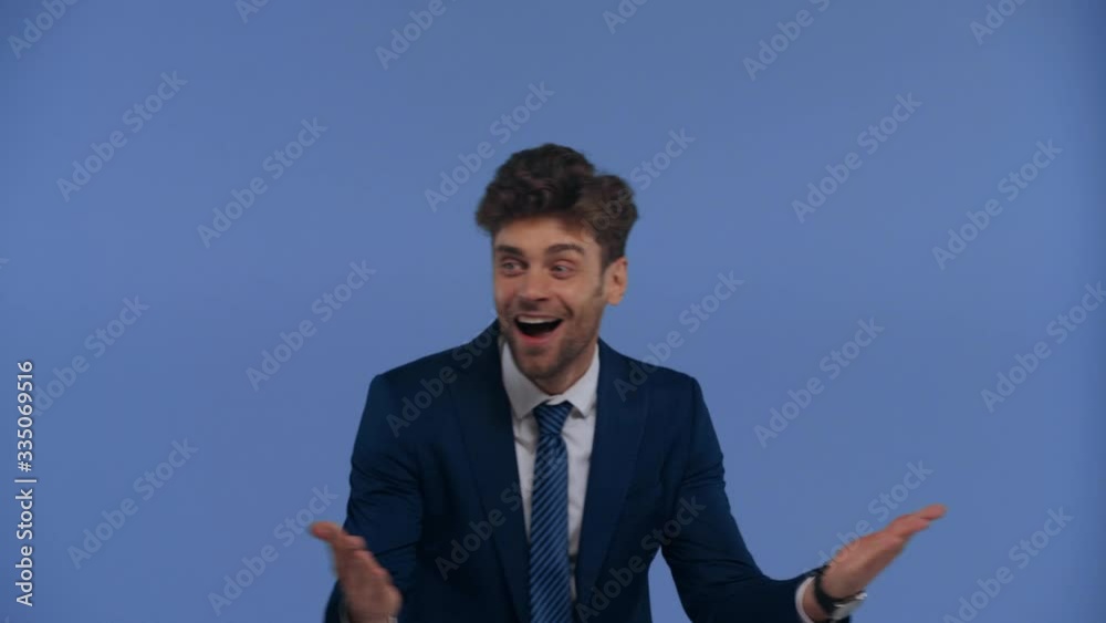 Shocked businessman showing thumbs up at camera isolated on blue Shocked businessman showing thumbs up at camera isolated on blue