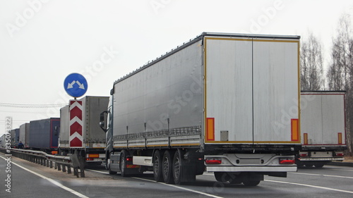 A many semi trucks queue on control point at spring dayback view, international cargo delivery traffic problem, illustration concept
