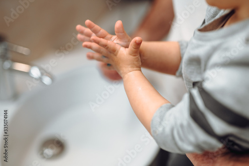 Little toddler using antimicrobial soap, washing hands with father at home