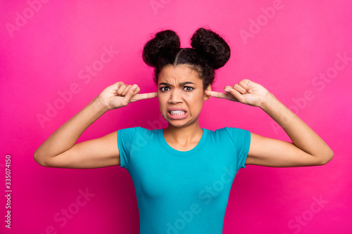 Closeup photo of crazy dark skin lady two buns hold fingers inside ears negative facial expression can't stand terrible sound wear blue casual t-shirt isolated bright pink color background © deagreez