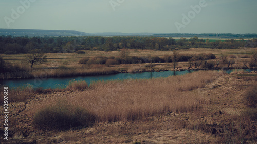 A quiet river in a green rural area. Beautiful landscape with a river with calm water, located next to a spring forest in nature. A narrow, winding river that runs through a grove of trees.