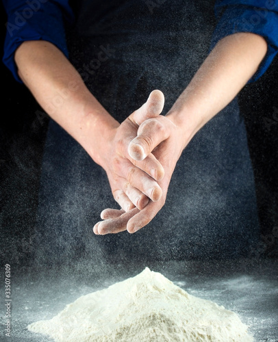 Hands of a man working with flour. Cooking process. Dark background.