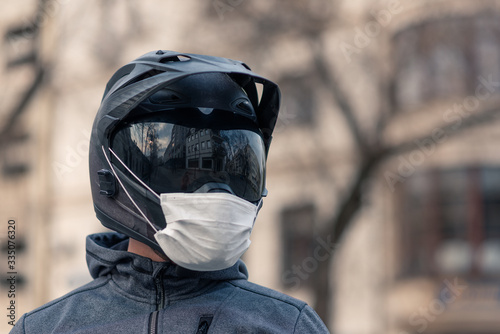 portrait of a man in a helmet. on a motorcycle helmet a white medical mask. photo on the street against the background of houses. coronavirus, disease, infection, quarantine, covid-19