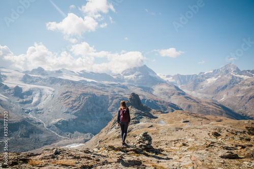 Girl with backpack standing on the rock with beautiful Swiss Alps covered in snow in background