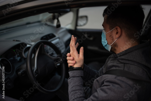 A man sits car and washes his hands with antiseptic gel. healthcare concept in car. The mask is white on the face. coronavirus, disease, infection, quarantine, covid-19 © Evghenii Blanaru