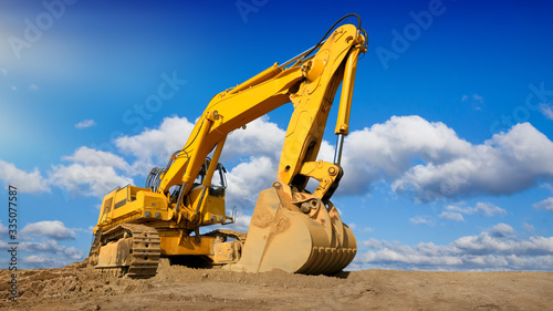 Big excavator on new construction site, in the background the beautiful blue sky with white clouds