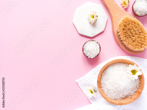 Spa flatlay composition. Sea salt, bath towel, massage wooden brush, flower on pink background. Copyspace, top view. Home care concept, relax and rest