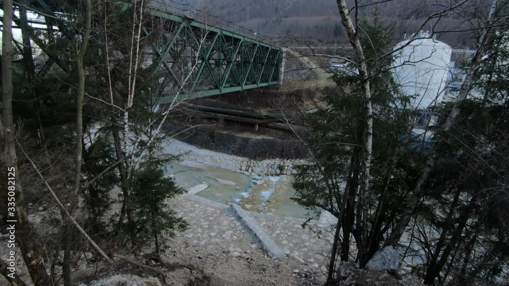 Left pan view of a green bolted railroad steel bridge support structure connected to a stone pillar over a river