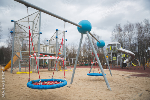 The playground in the city park is fenced with warning tapes in red and white. Coronavirus pandemic covide 19 worldwide. Self-isolation and measures to prevent the spread of the virus.