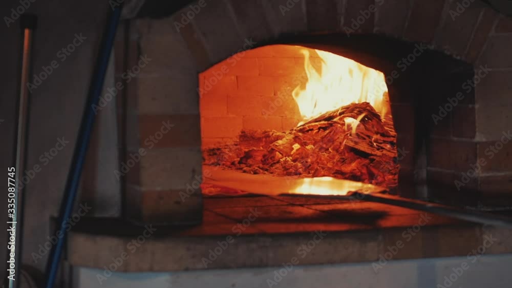 Pizza in the oven. A fire is burning in the oven. Checks pizza for