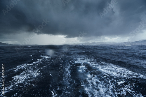 Fototapeta Naklejka Na Ścianę i Meble -  The view of the stormy sea and mountains from the sailboat, Path from foam after the boat, splashes from under the boat, rainy weather, dramatic sky