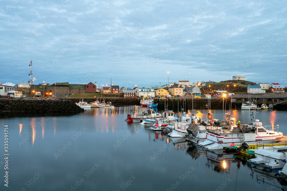 Fishing boats in Stykkisholmur city harbour in west Iceland during blue hour. City lights reflects in the calm water.