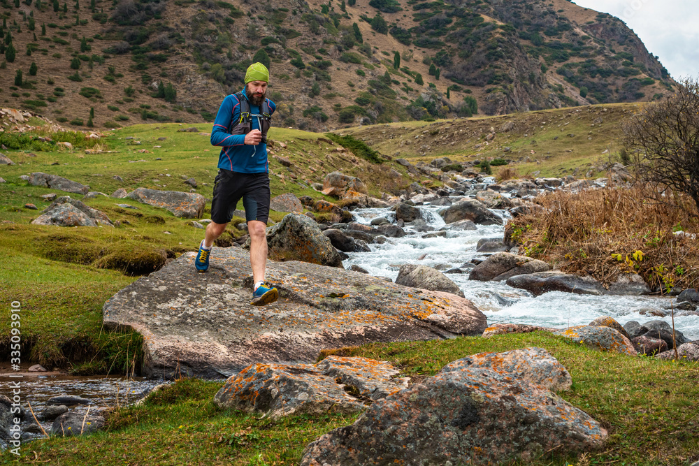 Runner guy is jogging in the highlands. Athlete runs near a mountain river. Man is training outdoors. Trail running