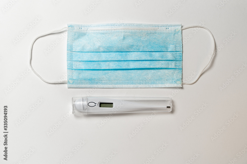 Surgical mask and digital thermometer on white background