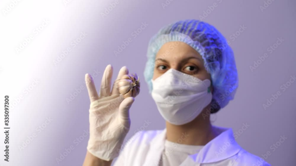 Cute female doctor in a medical protective mask holds garlic in hands. Coronavirus or COVID-19. Useful products for immunity