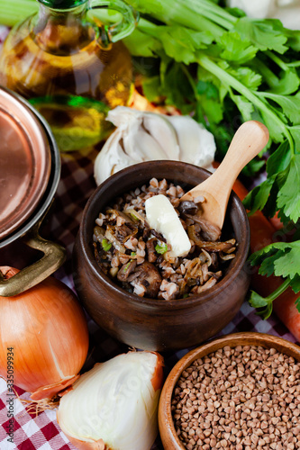 Traditional russian simple healthy meal  cooked buckwheat porridge with fried mushrooms  vegetables  butter in clay pot. Healthy food  low calories. Copper pan  wooden background  close up
