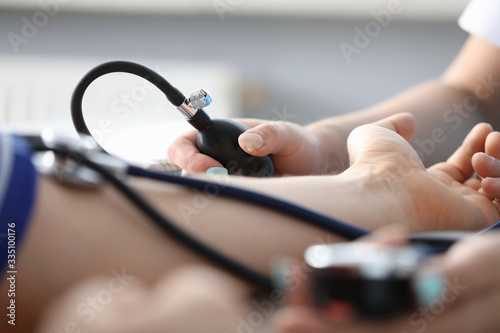 Close-up of persons hand on desk and doctor measuring blood pressure. Planned diagnostic. Modern equipment to examine circulation. Medicine and appointment concept