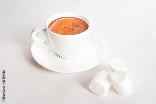 White cup of coffee on saucer and three marshmallows on white background. Minimalistic style. Coffee break.