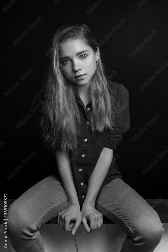 Black and white portrait of young stylish pretty sensual lonely girl in checkered shirt, jeans posing in studio while sitting and holding hands in front of her. her eyes are summed up with mascara Black and white portrait of young stylish pretty sensual lonely girl in checkered shirt, jeans posing in studio while sitting and holding hands in front of her. her eyes are summed up with mascara