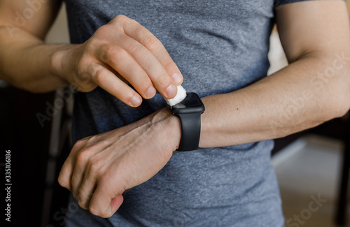 a man wipes an antiseptic against viruses and germs smart watch on his hand