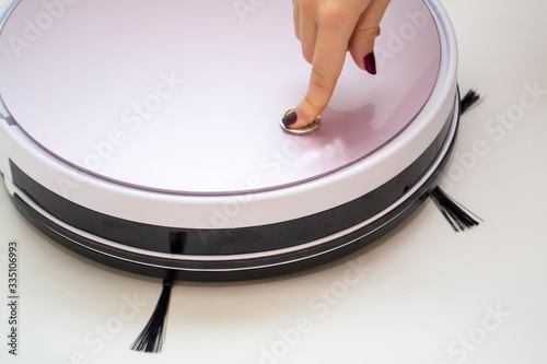 Finger presses a button on a robot vacuum cleaner