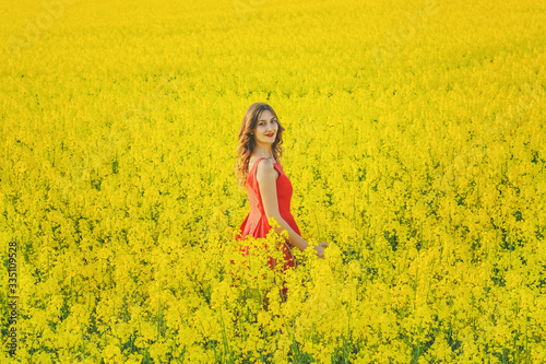 Young beautiful girl in a red dress close up in the middle of the yellow field with the radish flowers closeup