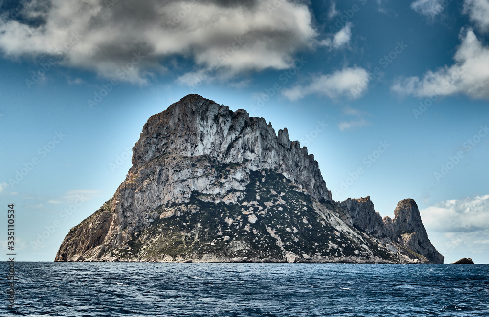 The Landscape of the balearic sea and improbable mountains, azure water, the storm sky, lonely buildings at tops of mountains, sail boat is on background The Landscape of the balearic sea and improbable mountains, azure water, the storm sky, lonely buildings at tops of mountains, sail boat is on background