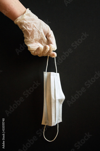 Hand in a transparent glove with a disposable medical mask on a black background. Concept: means of protection during coronavirus quarantine.