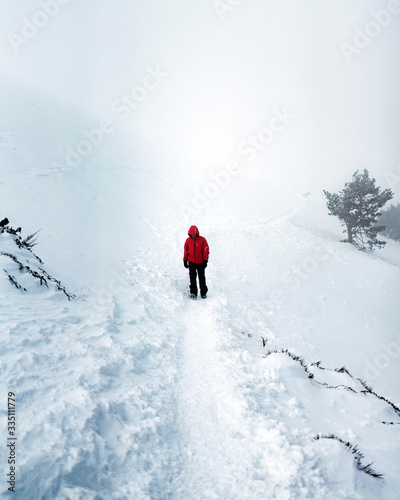 Man trekking in very snowy and misty mountain path with red jacket