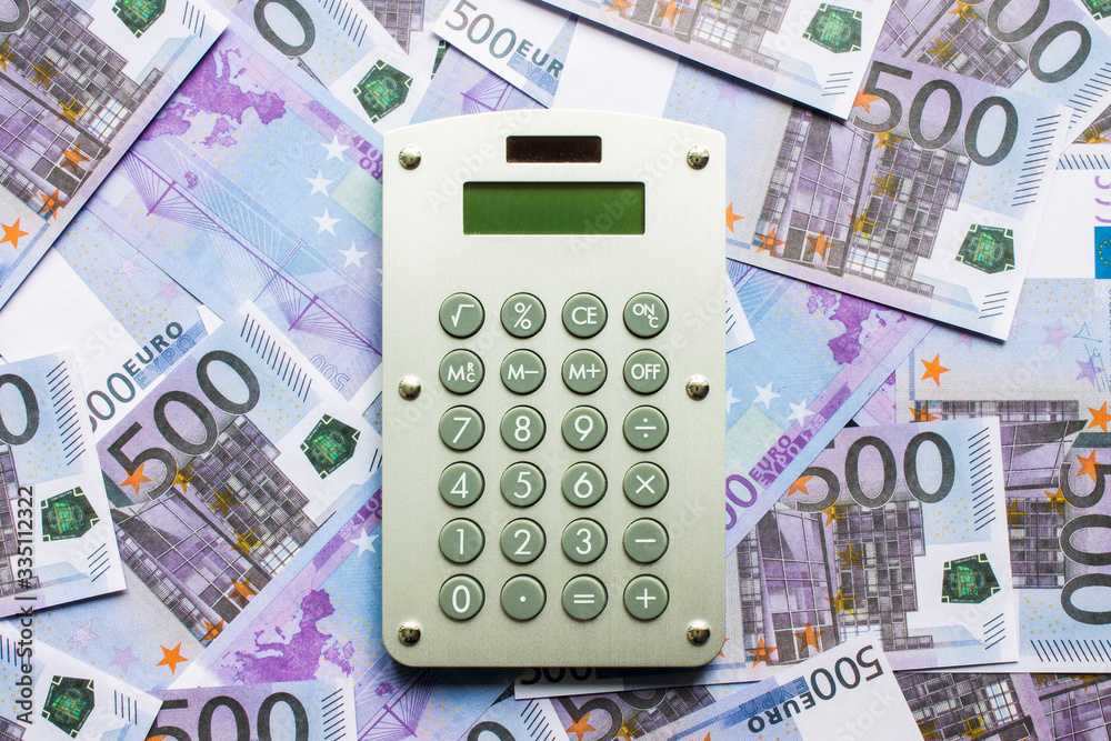 Calculator on a scattering of 500 Euro banknotes close-up flat lay.