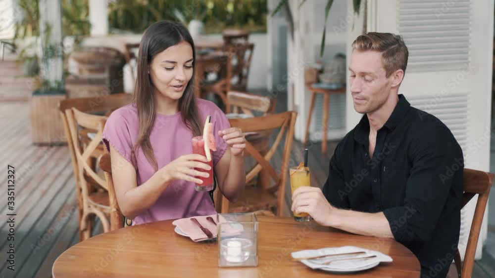 Young couple in cafe, guy and girl drinking fresh juices, talking, laughing Young couple in cafe, guy and girl drinking fresh juices, talking, laughing