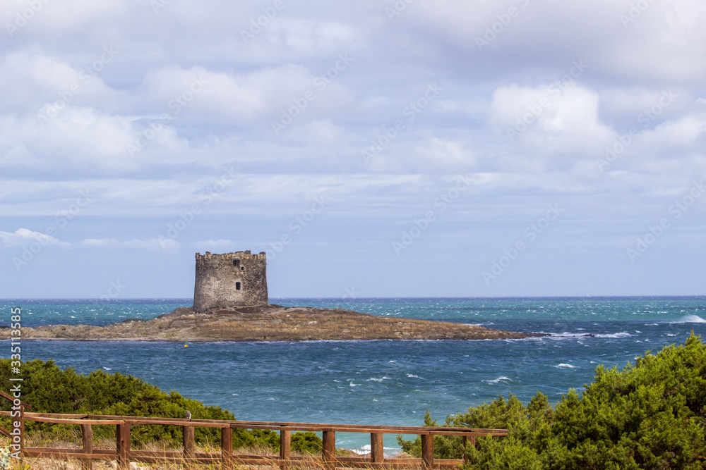 Summer view on the old aragonese tower in La Pelosa Beach.  Beautifull waves with foam, geen trees in Stintino, Sardinia, Italy