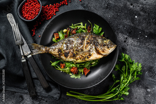 Baked sea bream fish with arugula salad and tomatoes. Black background. top view
