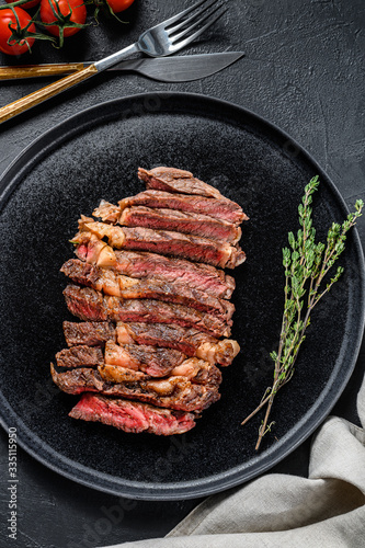 Sliced rib eye, ribeye steak on a plate with a sprig of thyme. black background. top view