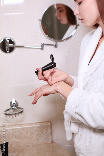 A young girl in the bathroom applies hand cream. The face is out of focus. Copy of the space.