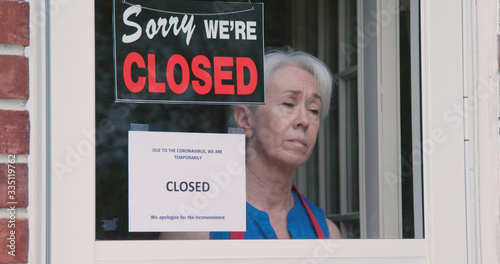 A worried mature small business owner turns the sign on her storefront from open to closed as a result of the shutdown issued because of the coronavirus.