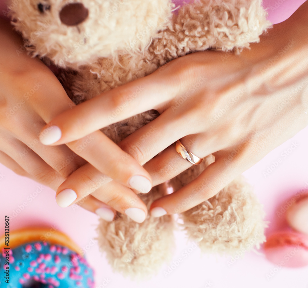 woman hands with manicure wearing wedding ring holdind teddy bear and macaroons on pink background woman hands with manicure wearing wedding ring holdind teddy bear and macaroons on pink background