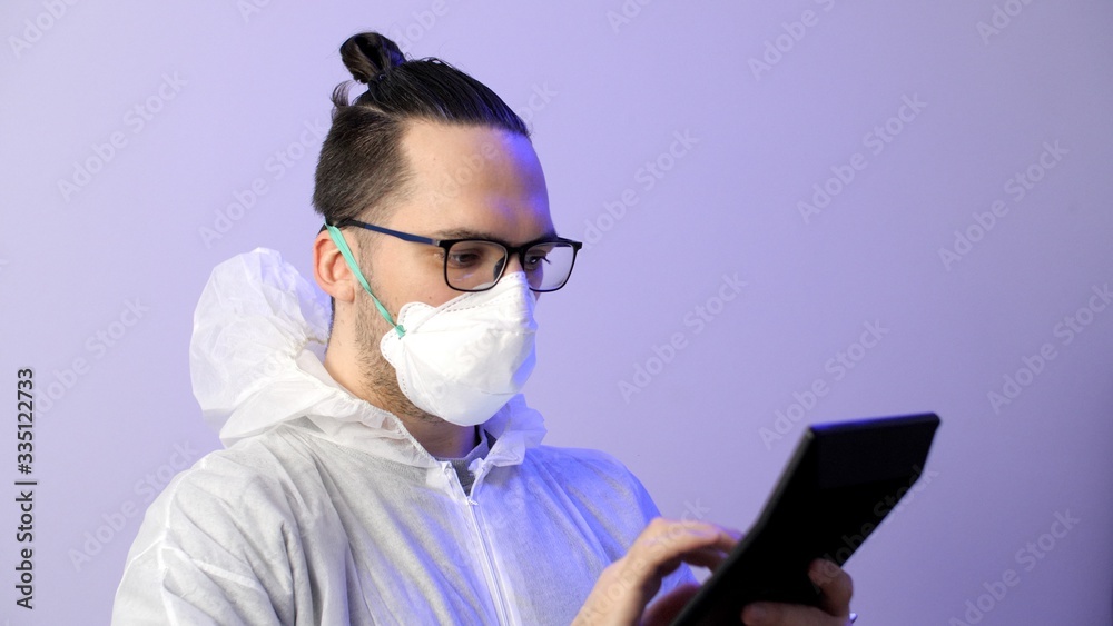 Man in a protective surgical suit and protective medical mask counts on a calculator. Budget for medicine, salary of doctors. Coronavirus or COVID-19 prevention.